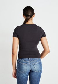 Sort kortærmet tætsiddende t-shirt parret med lyse denim jeans, der har to baglommer og lige snit.