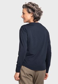 Marineblaues Langarmshirt mit Rundhalsausschnitt und elastischen Bündchen, kombiniert mit beigen Hosen. Baumwollstoff mit glatter Textur.