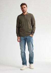 Olivgrünes Langarm-Poloshirt mit Zwei-Knopf-Leiste, kombiniert mit hellblauen Jeans und weißen Sneakern. Schlichtes Design, lockere Passform.