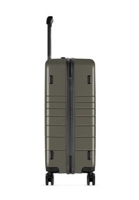 Hartschalentrolley in olivgrün mit horizontalen Rillen, schwarzem Reißverschluss und ausziehbarem Griff. Vier Räder für Mobilität und Stabilität.