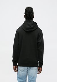 Sweatshirt preta com capuz e corte descontraído, apresentando um bolso canguru e punhos canelados, combinada com jeans azul claro. Design minimalista.