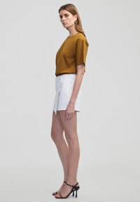 Korte mouwen, mosterdkleurig topje gecombineerd met witte shorts, met een aansluitend ontwerp en twee zijzakken. Zwarte sandalen met banden maken de outfit compleet.