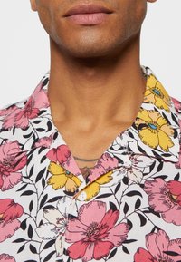 Bloemige short-sleeve shirt met roze, gele en witte bloemen op een witte achtergrond, met zwarte bladeren en een knoopcollar.