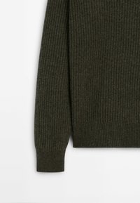 Manche et partie inférieure du torse d’un pull en maille côtelée vert foncé avec poignets ajustés sur fond blanc.