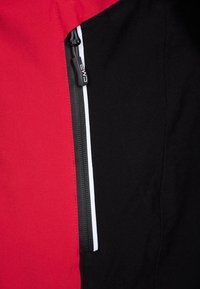 Sección de chaqueta roja y negra con un bolsillo con cremallera. La tela es suave, con colores contrastantes y un logo CMP en el tirador de la cremallera.