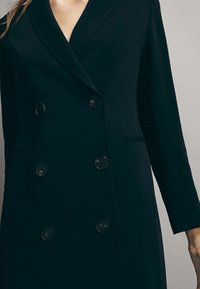 Schwarze doppelt knöpfbare Blazerjacke mit Reverskragen, ausgestattet mit sechs runden Knöpfen und langen Ärmeln. Glattes Material mit einer strukturierten Passform.