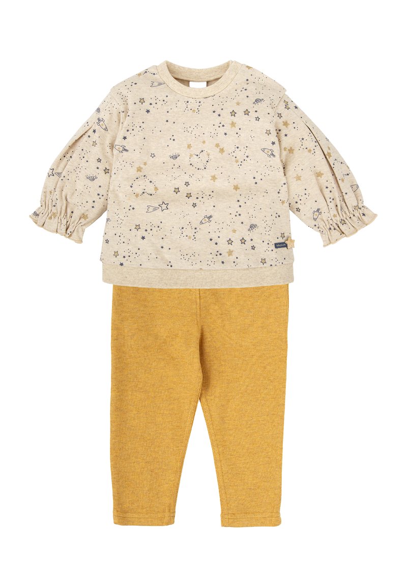 Camisa de manga larga beige con estampado de estrellas y planetas, combinada con pantalones amarillos mostaza. Tela texturizada con mangas fruncidas y cuello redondo.