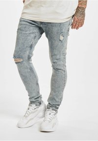 Lyseblå denim skinny jeans med slitte detaljer, med hull på knærne. Kombinert med hvite treningssko.