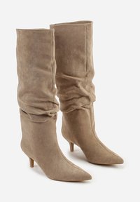 Bottes beige jusqu'au genou en daim doux, avec un design décontracté, un bout pointu et un talon aiguille de 6,5 cm. Texture lisse, détails minimalistes.