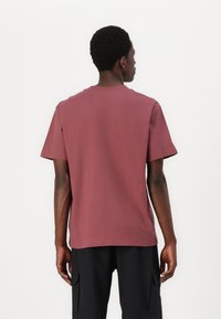Bordeauxfarbendes Baumwoll-T-Shirt mit kurzen Ärmeln, Rundhalsausschnitt und geradem Saum. Glatte Textur, lockere Passform und keine sichtbaren Muster oder Beschläge.