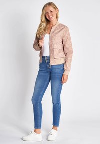 Bomber jacket in light pink with a subtle pattern, front zipper, and two pockets; paired with blue skinny jeans and white sneakers.