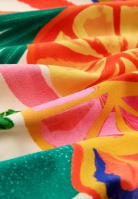 Gros plan d’un tissu coloré avec des motifs floraux et feuilles abstraits dans des tons verts, orange, rose, jaune et bleu.