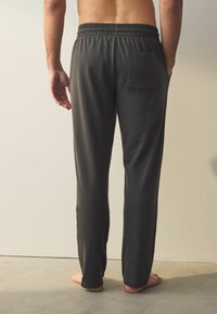 Pantaloni gri închis, cu croială lejeră, talie elastică și un singur buzunar la spate. Textură netedă și design cu picior drept, lungime până la gleznă.