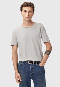 T-shirt grigio chiaro a maniche corte con scollatura rotonda, abbinato a jeans in denim blu e una cintura nera. Presenta un design semplice e una texture morbida.