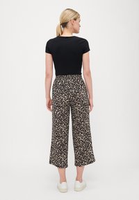 Svart kortermet topp kombinert med beige leopardmønstrede vide bukser, med elastisk midjebånd og hvite sneakers.