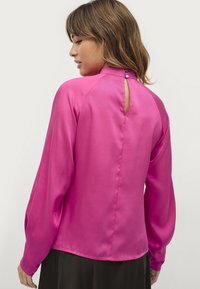 Langarm blouse in helder roze satijn met een hoge hals en een knoopsluiting op de rug, met een keyhole-detail.