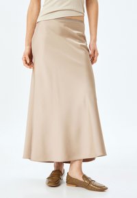 Beige satin maxiskørt med en glat tekstur, flydende design og subtil glans. Kombineret med brune teksturerede loafers.