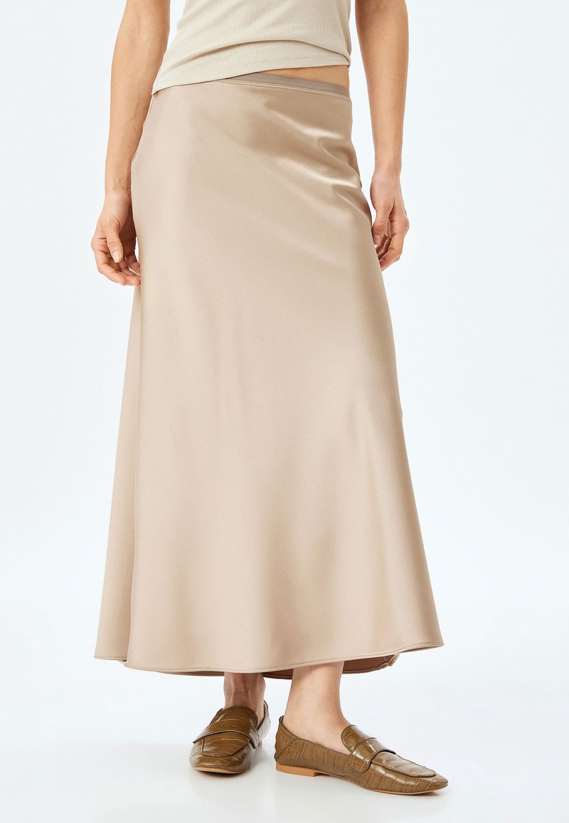 Beige satin maxiskørt med en glat tekstur, flydende design og subtil glans. Kombineret med brune teksturerede loafers.