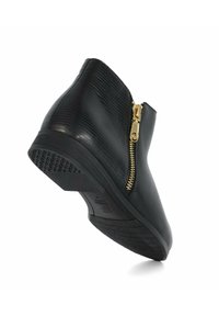 Bottine noire en cuir texturé, avec fermeture éclair latérale dorée, talon bas et semelle en caoutchouc, inclinée sur fond blanc.
