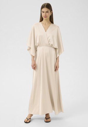 Maxi-Kleid aus leichtem beigefarbenem Satin mit V-Ausschnitt, weiten Ärmeln und gerafftem Bund. Glatte Textur mit schwingender Silhouette. Flip-Flops vervollständigen den Look.