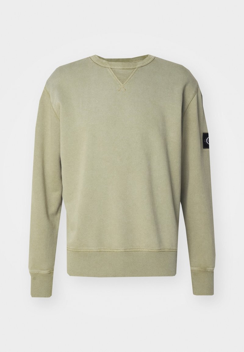 Felpa leggera beige con colletto rotondo, polsini e orlo a coste, con un piccolo patch nero sulla manica sinistra.