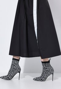 Bottes à talons hauts à motifs géométriques noir et blanc portées avec une jupe midi noire avec une bande centrale blanche.