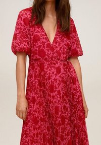 Robe rouge à fleurs avec manches bouffantes, décolleté en V, taille cintrée, jupe fluide et motif de roses délicat sur un tissu léger.