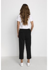 Zwarte broek met een ontspannen pasvorm, elastische tailleband, zijzakken en details van een achterzak, gecombineerd met een effen wit T-shirt en witte sneakers.