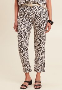 Luipaardprint broek in beige en zwarte stof, cropped bij de enkel, gecombineerd met zwarte hoge hakken. Bevat een gestructureerde riem en een gladde textuur.