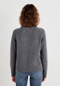 Szary sweter wykonany na drutach z okrągłym dekoltem i ściągaczem, z długimi rękawami i miękką teksturą. Noszony z niebieskimi dżinsami.