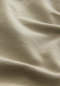 Tela beige con una superficie suave y ligeramente texturizada. Aparece suave con arrugas sutiles, lo que indica un material flexible y ligero.
