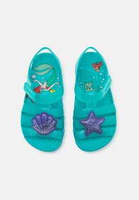 Tyrkis barne sandaler med glitrende lilla skjell og stjernedekorasjoner, med undervanns tegneseriefigurer inni.