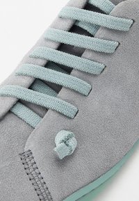 Gros plan de lacets tressés bleu clair noués sur des baskets en suède gris doux avec des coutures visibles et un bord de semelle texturé.