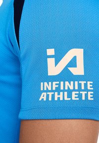 Vaaleansininen urheilu-paitamalli, jossa on teksturoitu kangas. Olkaissa mustat yksityiskohdat ja valkoista tekstiä: "INFINITE ATHLETE" logon kanssa.