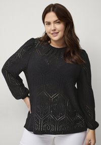 Zwarte blouse met lange, opbollende mouwen, voorzien van een geometrisch uitgesneden patroon en een ronde halslijn, gemaakt van textuurstof.