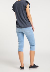 Mörkblå kortärmad topp med vita prickar, volangärmar, matchad med ljusblå korta jeans och svarta sneakers.