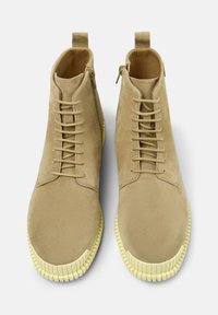 Beige suède enkellaarsjes met een rubberen zool. Ze hebben een vetersluiting aan de voorkant en een ritssluiting, met een gestructureerde gele buitenzool.