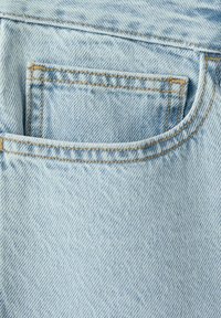 Tissu en denim bleu clair en gros plan montrant une petite poche avant de jean avec des coutures orange visibles.