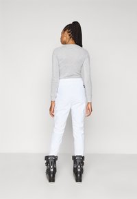 Γκρι μπλούζα μακρυμάνικη με εφαρμοστή σχεδίαση, σε συνδυασμό με λευκό παντελόνι σκι και μαύρες μπότες σκι. Απλές, καθαρές γραμμές και χωρίς εμφανή σχέδια.