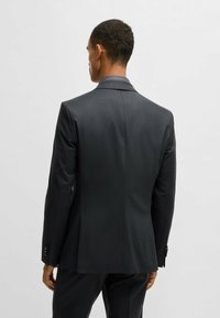 Giacca nera con una texture liscia, design a un bottone, revers classici e polsini con bottone, vista da dietro.