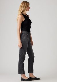 Top a fascia nera a costine abbinato a jeans grigi con vita media e taglio dritto, con rivetti in ottone e una toppa in pelle marrone sul retro. Ballerine nere.