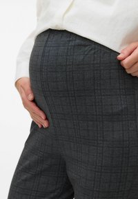 Pantalons à carreaux gris en tissu texturé, dotés d'une taille haute et d'un emplacement latéral pour les mains afin de démontrer l'ajustement.