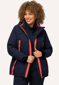 Marinblå jacka med orange detaljer, dragkedja, huva och sidofickor; tillverkad av ett slätt, texturerat tyg, designad för komfort och värme.