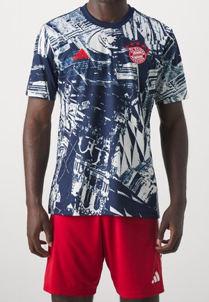 Homme portant un maillot abstrait bleu marine et blanc du FC Bayern Munich avec un logo Adidas rouge, assorti à un short rouge Adidas.