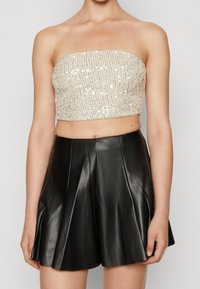 Beżowy crop top bez ramiączek ozdobiony cekinami, zestawiony z wysokim, rozkloszowanym czarnym skórzanym spódnicą, charakteryzującą się gładką teksturą i plisowanym designem.