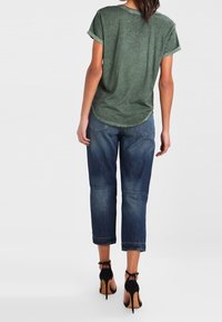 Camiseta verde de manga corta combinada con jeans de mezclilla azul cortos. Los jeans tienen un aspecto ligeramente desgastado y con dobladillos enrollados. Sandalias de tacón alto negras.