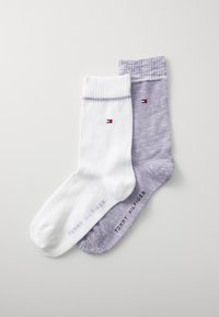 Zwei Paar Socken: eine weiße mit geripptem Bündchen und Logo, und eine lila mit einer gesprenkelten Textur, beide mit dem Markennamen "Tommy Hilfiger".