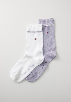 Zwei Paar Socken: eine weiße mit geripptem Bündchen und Logo, und eine lila mit einer gesprenkelten Textur, beide mit dem Markennamen "Tommy Hilfiger".