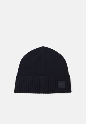 Gehaakte marineblauwe beanie muts met een geribde rand en een vierkante logo patch. Zachte textuur, strakke pasvorm die naar de bovenkant toe taps toeloopt.