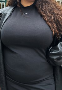 Svart Nike polotröja med en slät textur och ett figurnära snitt, lagd under en svart läderjacka med en mjuk yta.